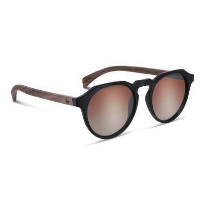 anteojos de sol hexagonales polarizados con patas de madera de hombre y mujer. vista frontal de gafas polarizadas de color negro matte con lentes de color degrade cafe con tratamiento espejado vista angulada con patas de madera natural de nogal #color-marco_negro