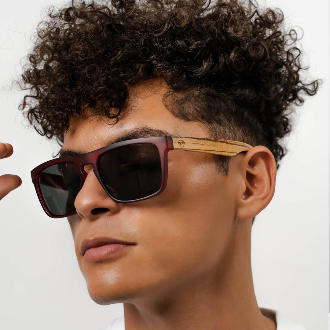 Un modelo men pelo rulo mirando in 45 grados hacia the camara with sunglasses rectangular red with lenses oscuras and wooden temples natural Bonoboss #color_wine