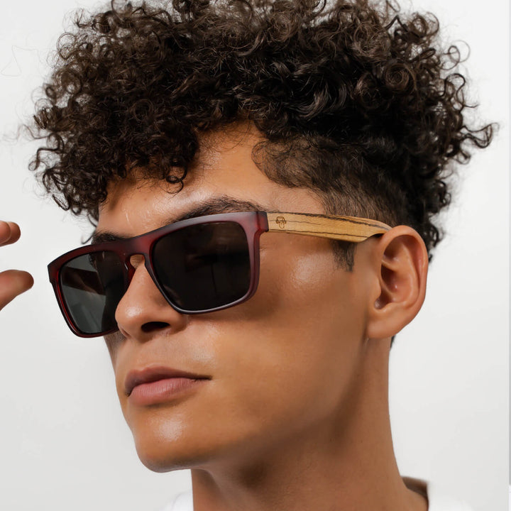 Un modelo men pelo rulo mirando in 45 grados hacia the camara with sunglasses rectangular red with lenses oscuras and wooden temples natural Bonoboss #color_wine