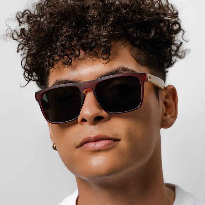 Un modelo men pelo rulo mirando in 25 grados hacia the camara with sunglasses rectangular red with lenses oscuras and wooden temples natural Bonoboss #color_wine