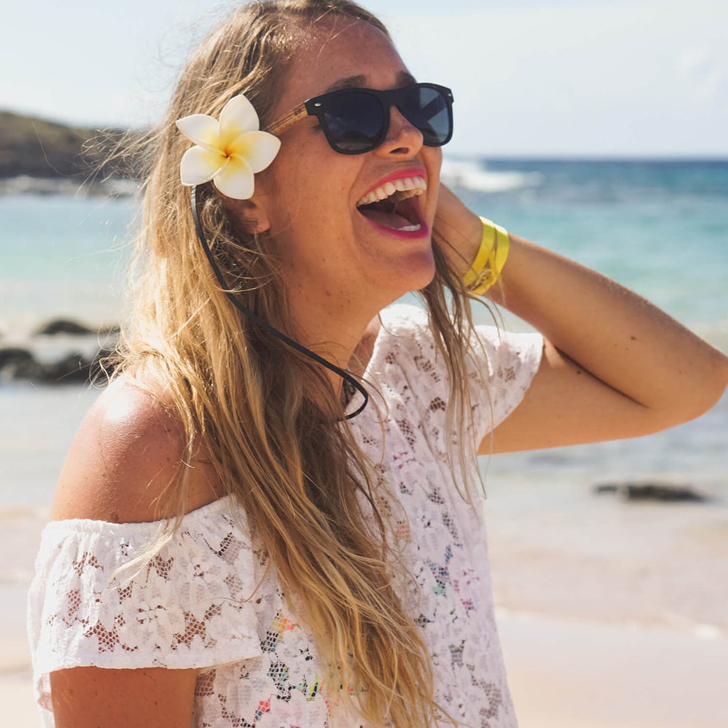mujer de cara redonda grande sonriendo y usando gafas o anteojos de sol polarizados con patas de madera reciclada o sustentable en la playa