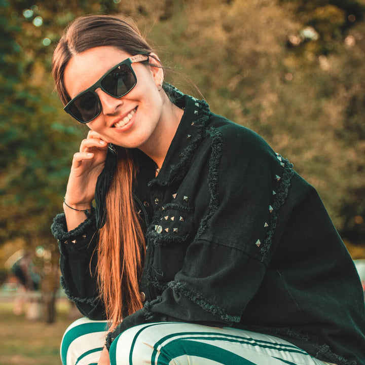 Una women sonriendo mirando a the camara in 45 grados pelo liso with chaqueta negra desgastada with tachas with sunglasses polarized black hecho with recycled plastic and wooden temples natural Bonoboss #color_negro