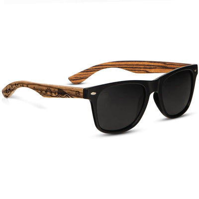 anteojos o gafas polarizadas de color negro con patas o varillas de madera natural reciclada sustentable. Vista angulada madera de zebrano y anteojo o marco de color negro polarizado para hombre y mujer con diseño de olas y de surfista